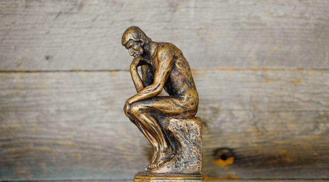 A small bronze statue of a thinker sitting on a pedestal, contemplating.