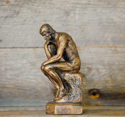 A small bronze statue of a thinker sitting on a pedestal, contemplating.