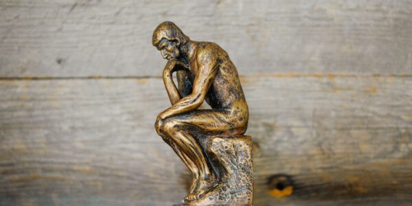 A small bronze statue of a thinker sitting on a pedestal, contemplating.