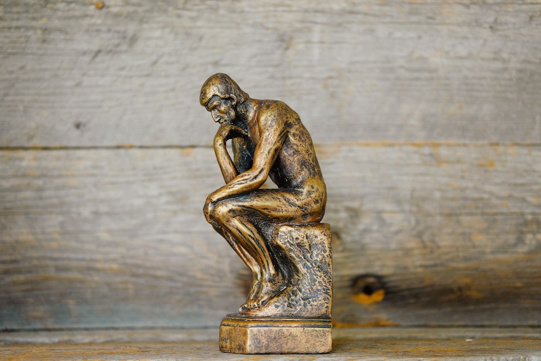 A small bronze statue of a thinker sitting on a pedestal, contemplating.